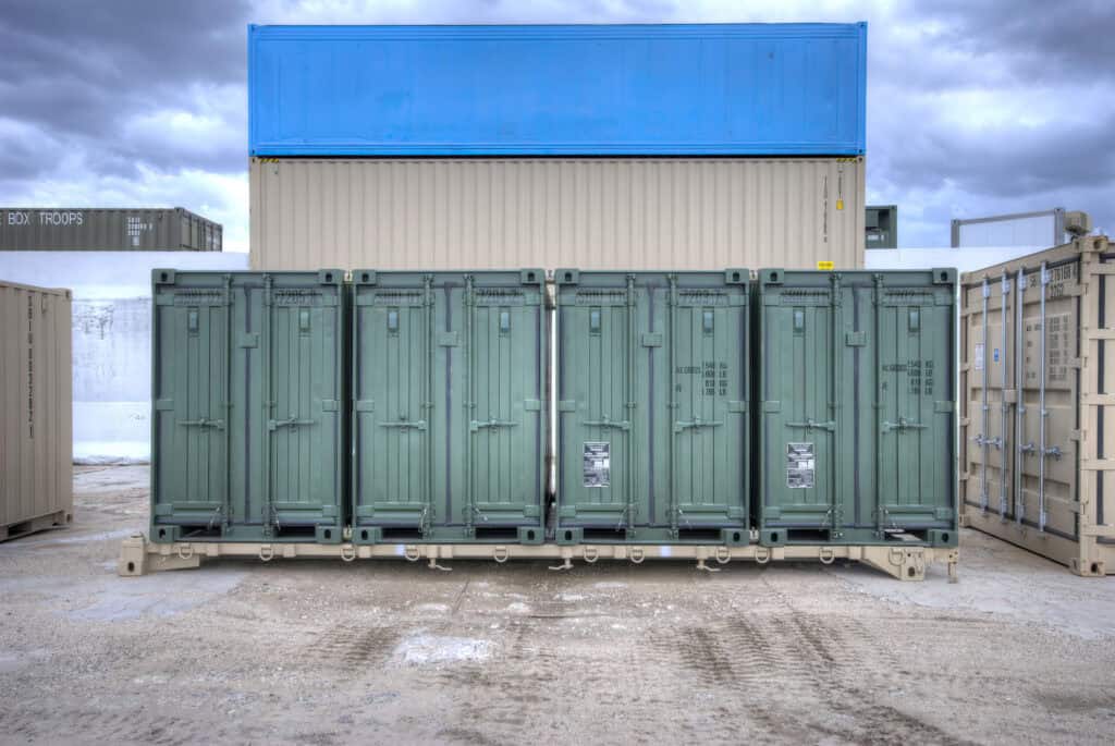 Row of green 20ft containers with a blue container stacked on top at a depot