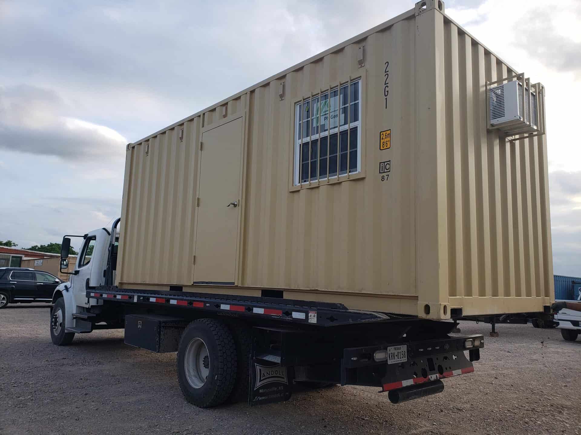 Beige container office being delivered on a tilt-bed truck