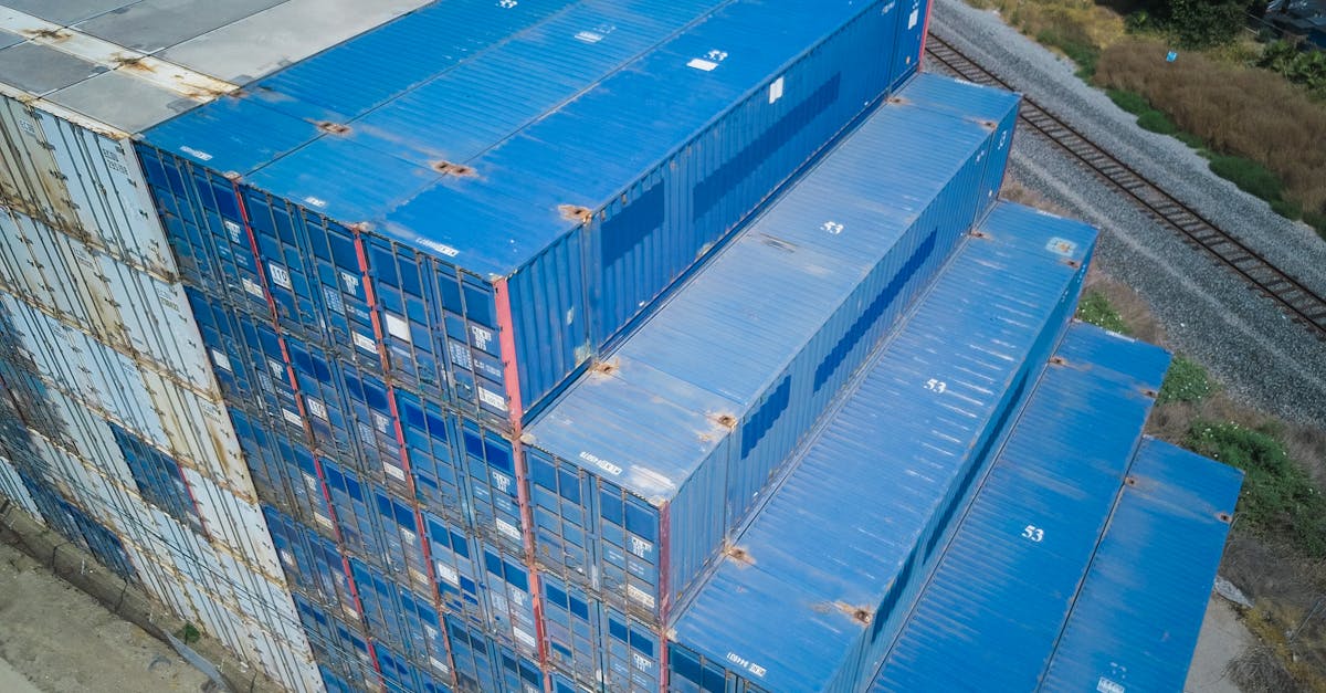Aerial view of blue shipping containers stacked beside a rail line