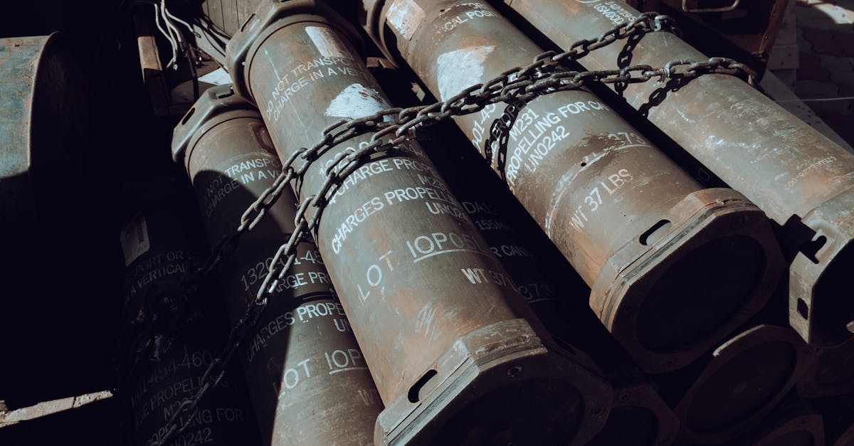 Rusty metal cylinders chained together in a dark industrial yard with weathered surfaces.