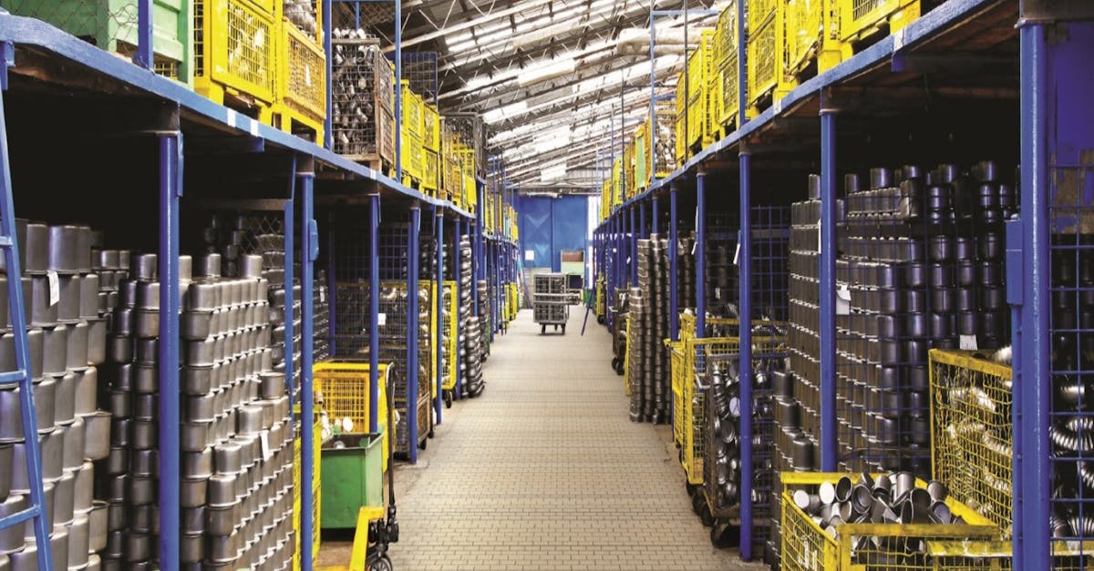 Long warehouse aisle with blue shelving, yellow crates, and stacked metal components on both sides.