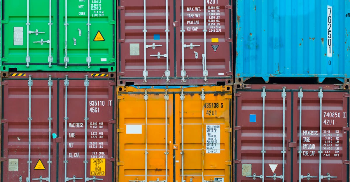 Colorful stacked shipping containers in green, red, orange, and blue with metal doors and latches in a yard.