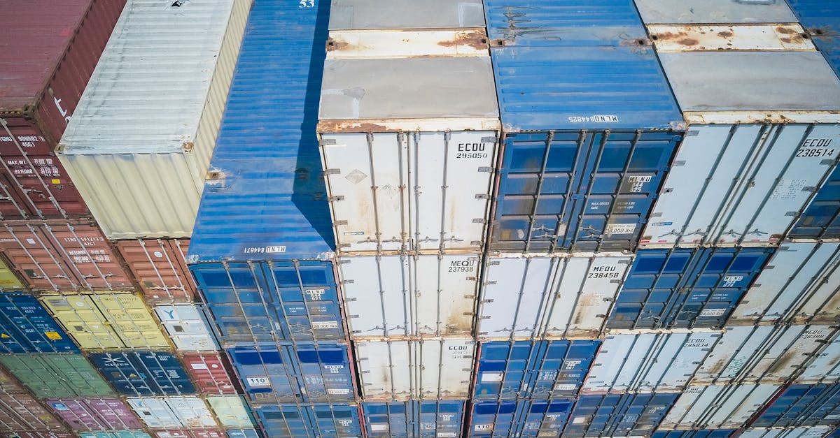 Aerial view of stacked shipping containers in blue, grey, and red, forming a grid pattern.