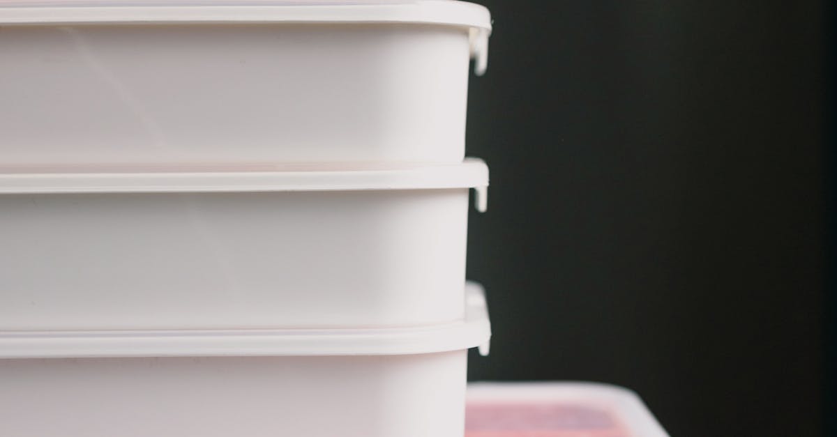 Stack of white plastic food storage containers with lids stacked vertically against a dark background.