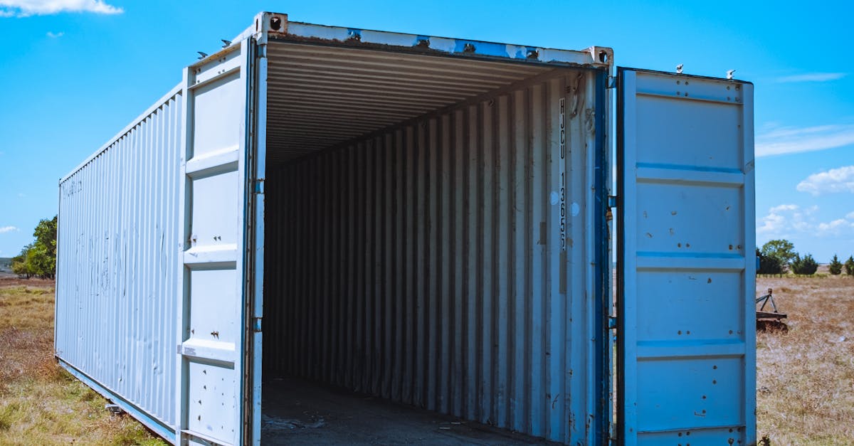 Open blue shipping container in a dry rural field with doors wide open, under a bright blue sky.