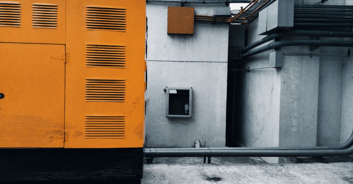 Industrial machinery in a concrete utility room with bright orange panels and exposed pipes on the right side of the image.