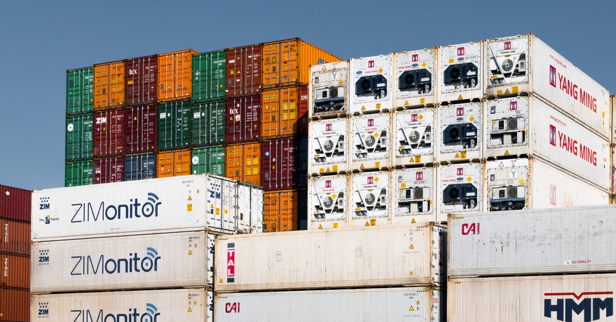 Stacks of colorful intermodal shipping containers stacked high under a clear blue sky at a cargo yard, ready for transport around the world.