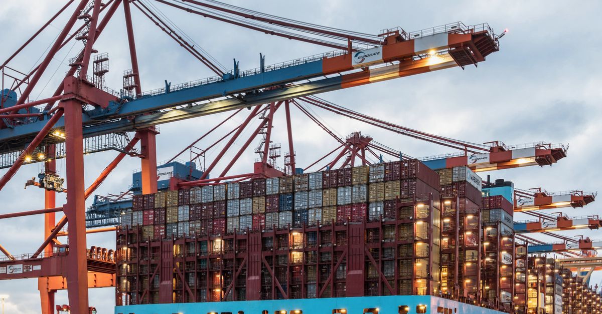 Container ship at a busy port with red gantry cranes and stacked cargo containers above the deck edge.