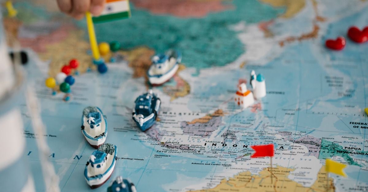 Miniature boats and colorful pins placed on a world map, suggesting travel planning or navigation ideas across continents.