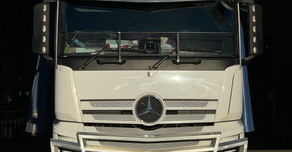 Front view of a white Mercedes-Benz semi-truck with its emblem centered on the grille and large bumper, dark background behind it.