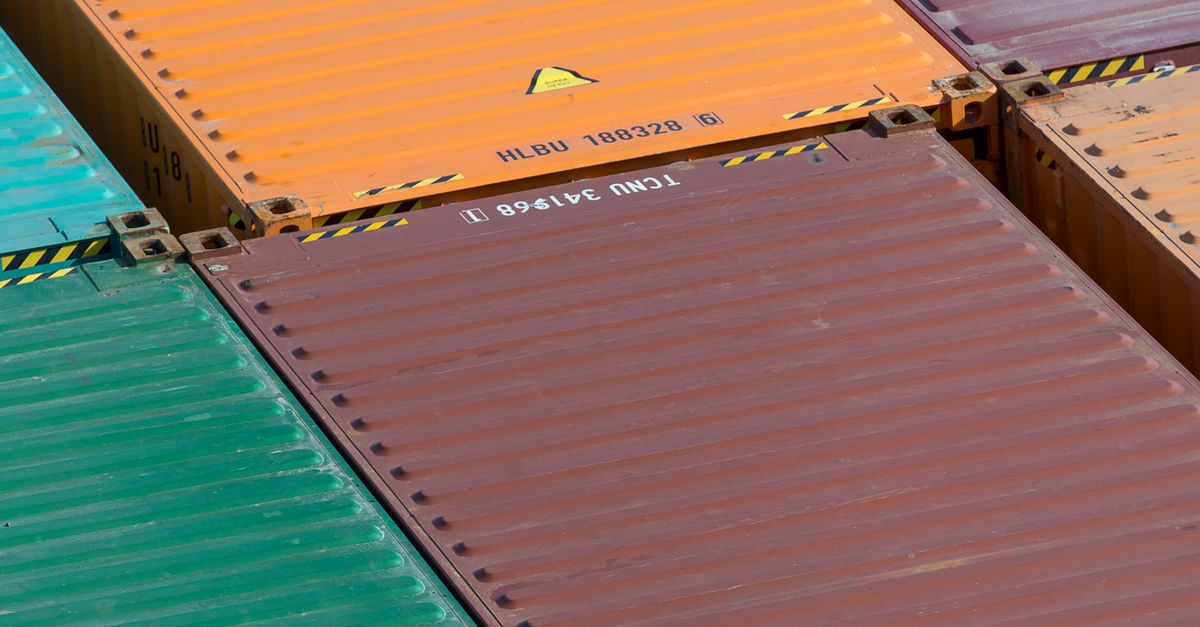 Top-down view of stacked metal shipping containers in green, orange, and brown colors with corner fittings and striped edges.