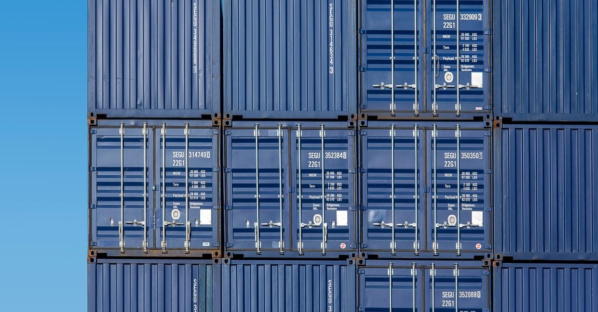 Stack of dark blue shipping containers with closed doors under a clear sky