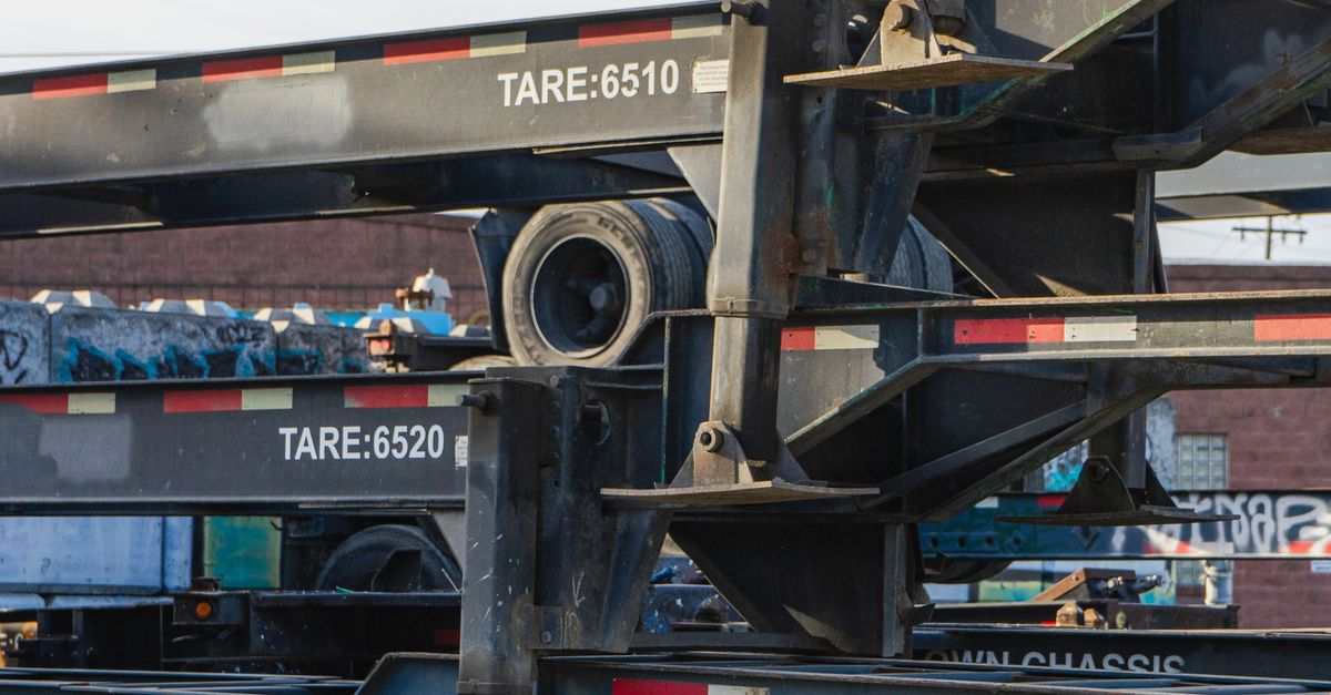 Stacked flatbed trailer frames with visible tires and graffiti in the background, showing tare labels (6510, 6520).