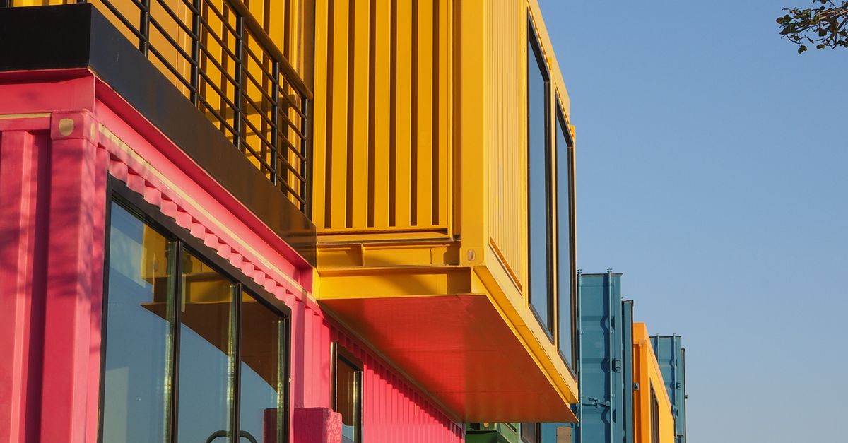 Exterior view of a colorful modular building with pink and yellow panels and large windows under a blue sky