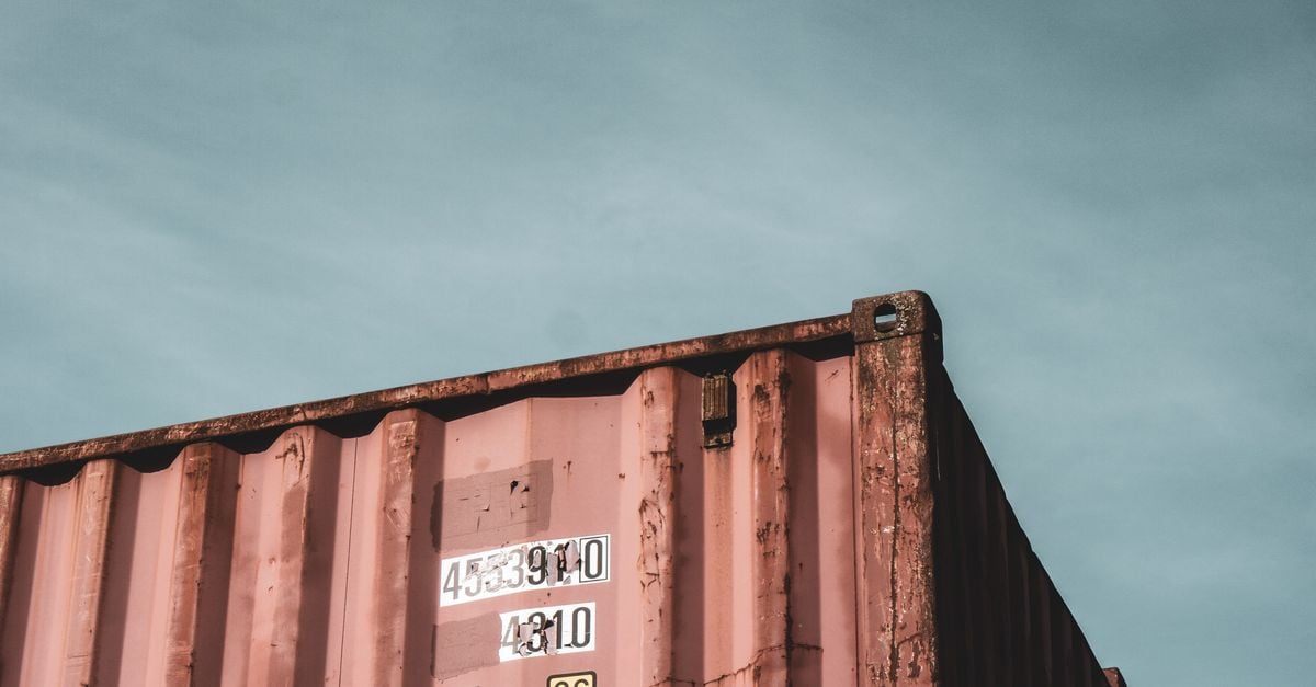 Corner of a weathered red shipping container against an overcast sky