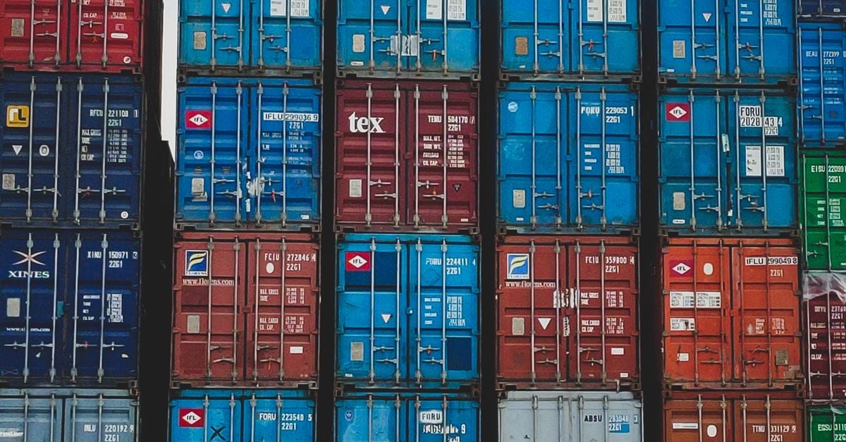 Stacks of colorful shipping containers in a storage yard (blue, red, green).