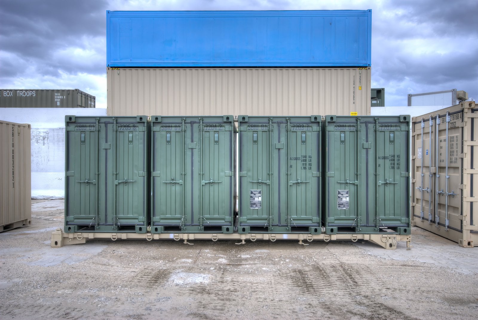 Four green quadcon containers coupled into a 20ft set on a tan frame in a container yard